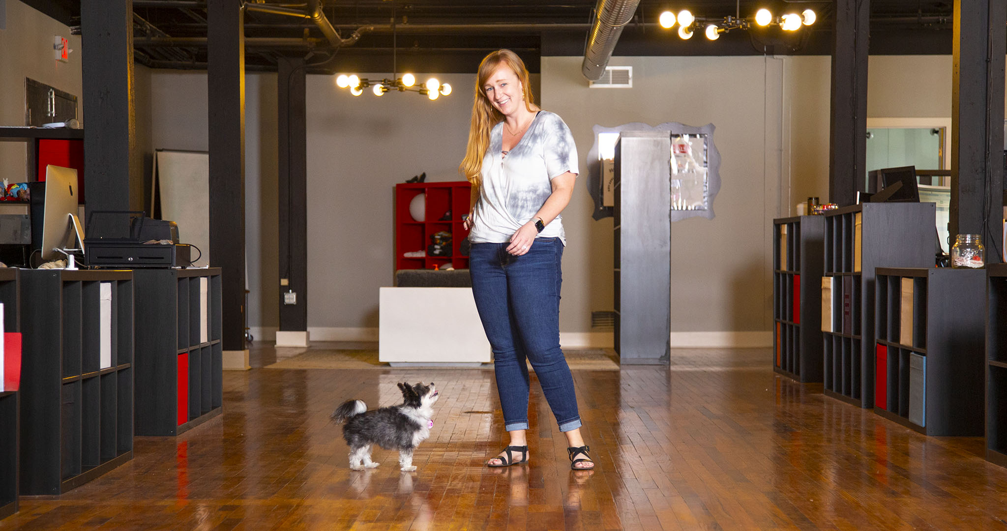 wide shot of Alicia Anderson standing in the middle of the office with her small black and white dog at her feet