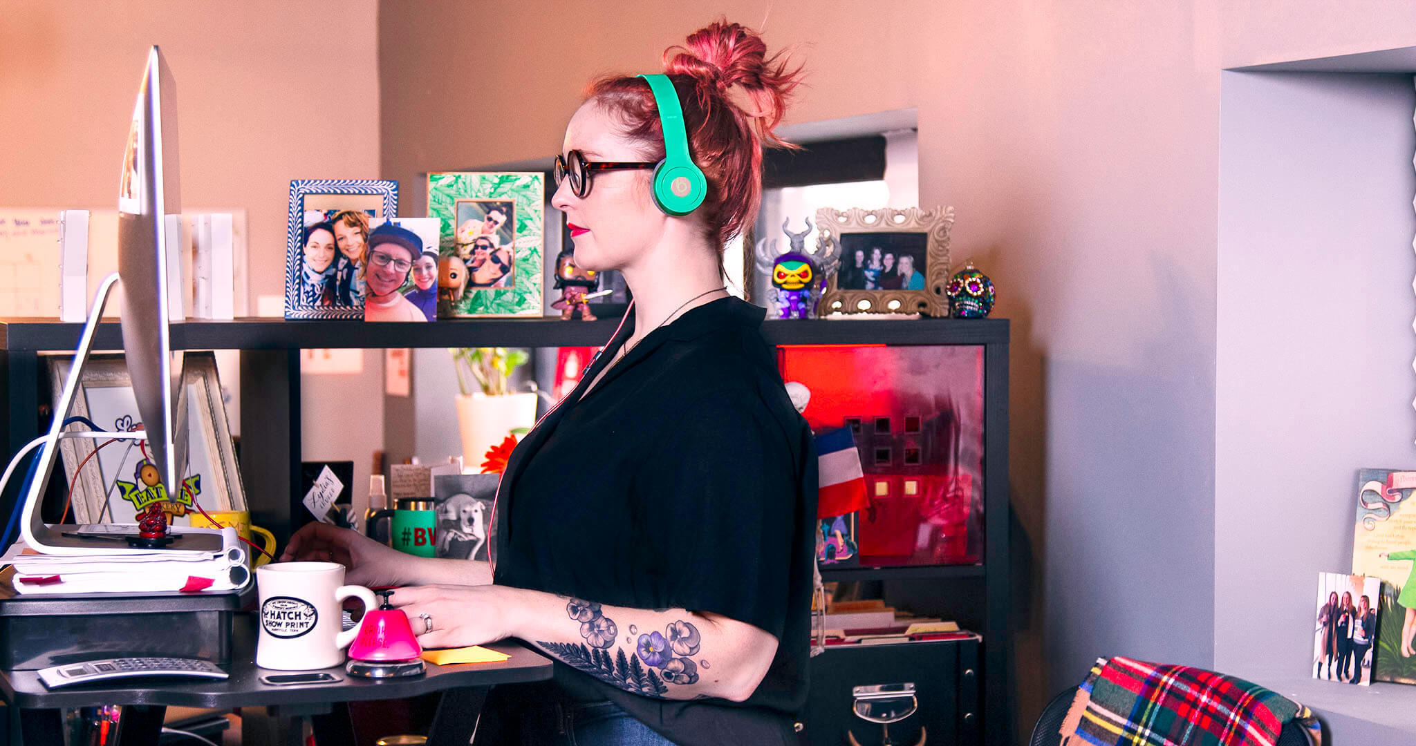 wide shot of Lydia Sax working at her standing desk with brightly colored headphones on