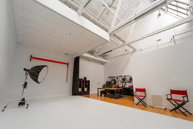 Professional photography studio with lighting equipment, director chairs, workstation with monitors, and backdrop setup