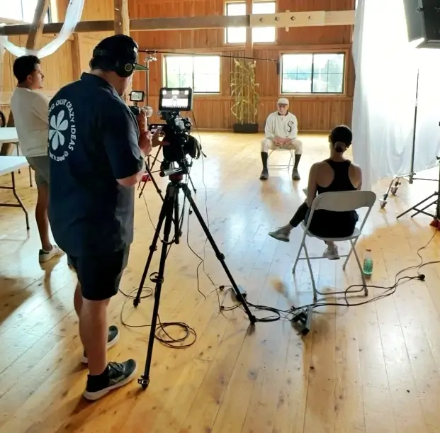 Behind-the-scenes video production in a wooden studio space with crew operating camera equipment and interviewing a subject