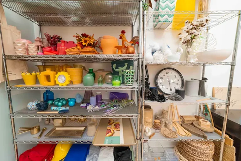 Wire shelving unit displaying colorful home decor items including vases, candles, decorative balls, flowers, a clock, woven baskets, and fabric storage boxes organized across multiple shelves